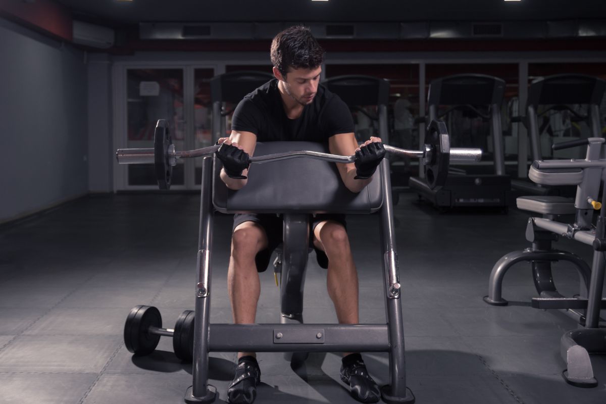 Man doing barbell curl on preacher bench.